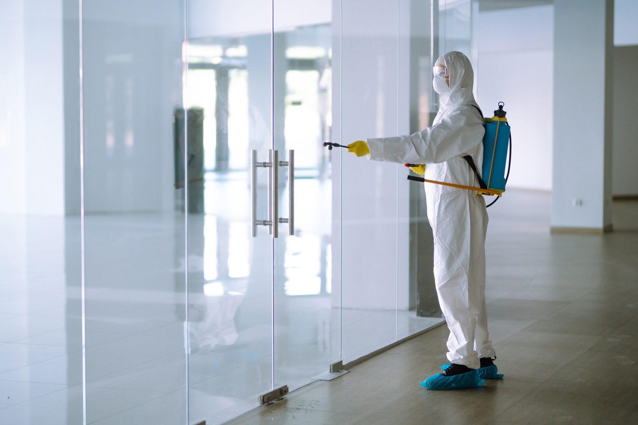 Person disinfecting glass door in protective suit.