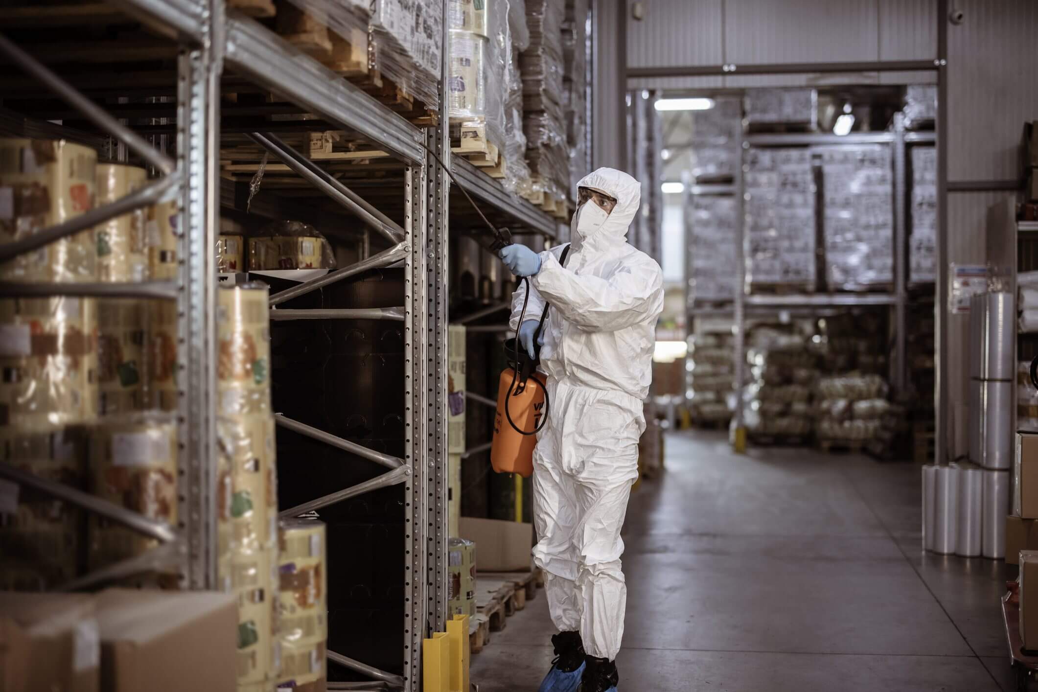 Person in protective suit inspecting warehouse shelves.