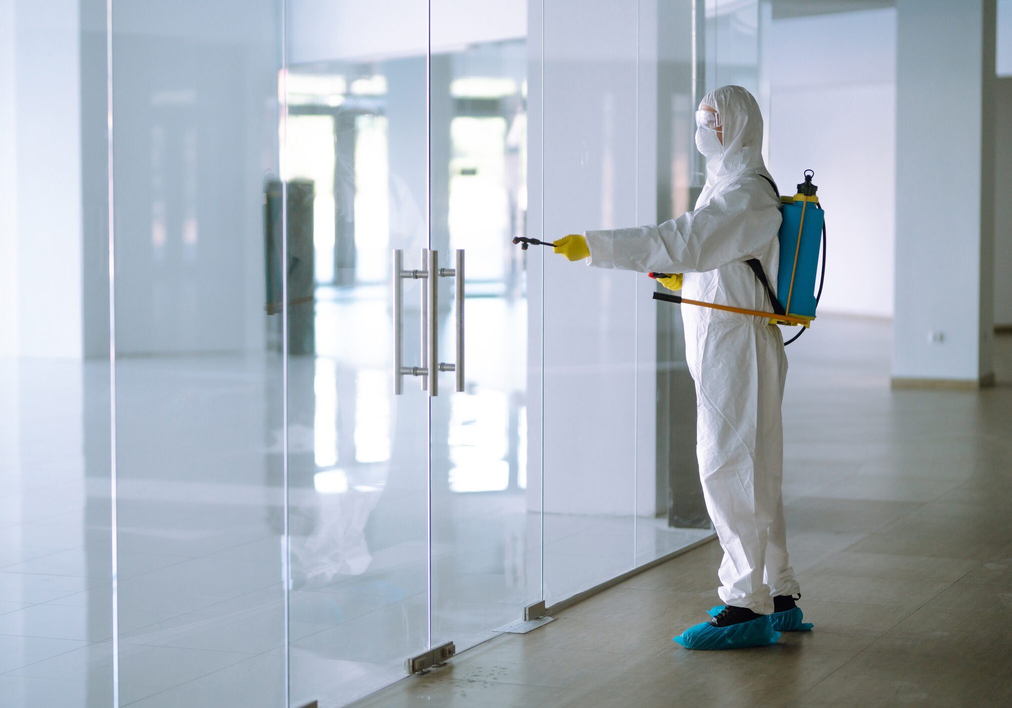Person disinfecting glass door in protective suit.